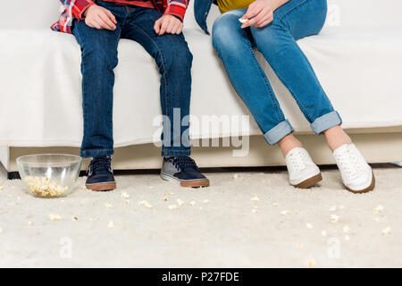 cropped shot of mother and kid sitting on couch with messy spilled popcorn on floor Stock Photo