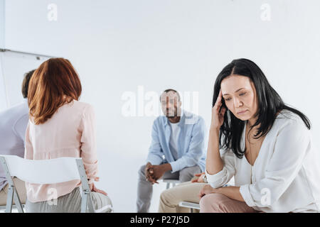 depressed asian woman looking down and multiethnic group sitting behind Stock Photo