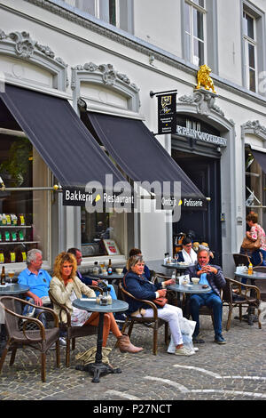An attractive young lady sits at a table outside a popular café restaurant in the city centre Bruges or Brugge, Belgium Stock Photo