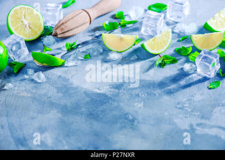 Summer drink header with mojito cocktail ingredients, mint, lime and ice cubes. Lemon reamer or juicer on a gray stone background with copy space. Stock Photo