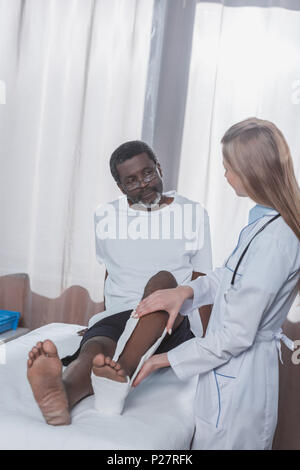 Doctor putting on plaster cast on injured african american patient leg in the hospital Stock Photo