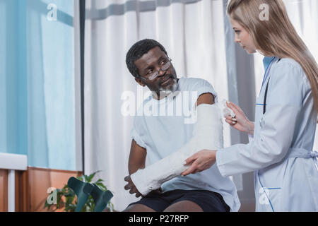 doctor bandaging african american patient hand with plaster cast in the clinic Stock Photo