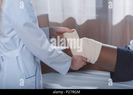 Cropped image of doctor putting on elastic bandage on african american patient knee Stock Photo