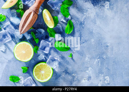 Summer drink header with mojito cocktail ingredients, mint, lime and ice cubes. Lemon reamer or juicer on a gray stone background with copy space. Stock Photo