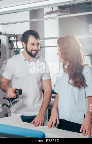 smiling young dry cleaning workers ironing clothes Stock Photo