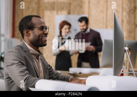 happy african american architect working with computer at modern office while his colleagues discussing contract Stock Photo