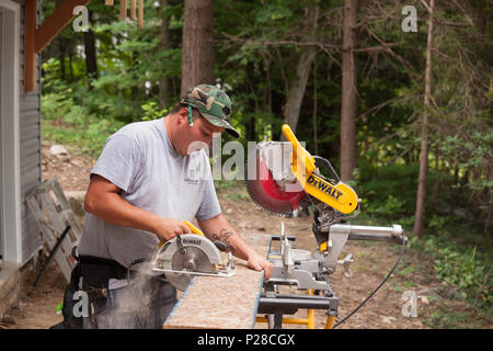 A construction worker using a handheld circular saw to cut a wooden plank. Stock Photo