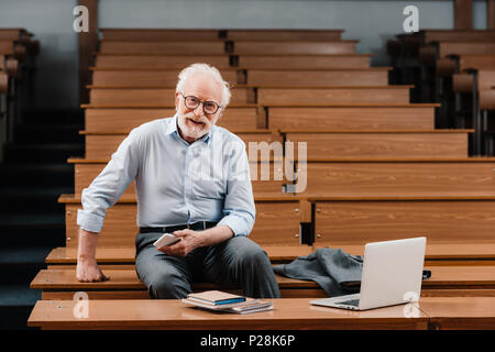 smiling grey hair professor sitting in empty lecture room Stock Photo