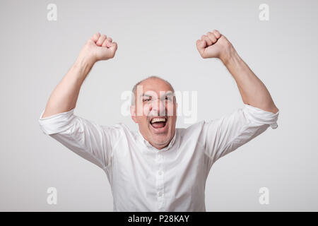 Portrait of mature european man with fists up. He is celebrating winning. Stock Photo
