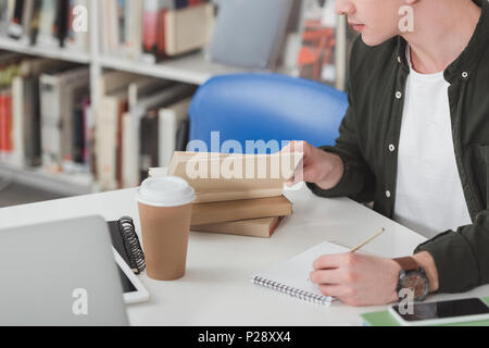 cropped image of student reading book and making notes in library Stock Photo