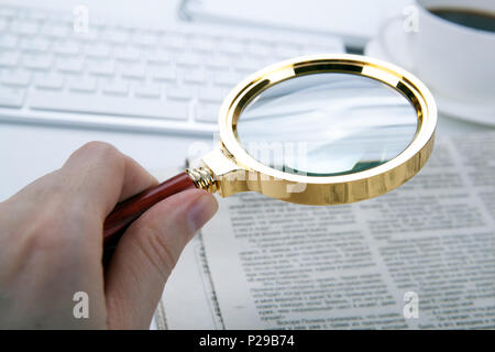 man's hand holds a magnifying glass over a newspaper font Stock Photo