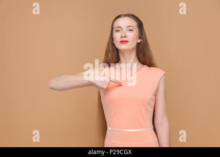 its me. proud woman pointing herself. portrait of emotional cute, beautiful woman with makeup and long hair in pink dress. indoor, studio shot, isolat Stock Photo