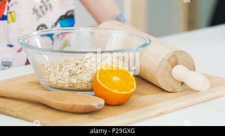 Oatmeal in glass bowl and orange with wooden rolling pin for cooking biscuits Stock Photo