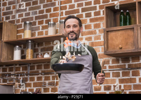 handsome man tossing up vegetables on frying pan Stock Photo