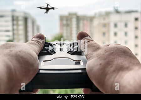 In the foreground remote control drone in his hands. In the background blurred background with drone and multi-storey houses. Stock Photo