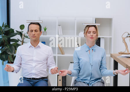 businesspeople meditating with books on head at modern office Stock Photo
