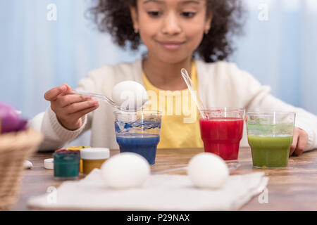 african american child painting easter eggs in glasses with paints Stock Photo
