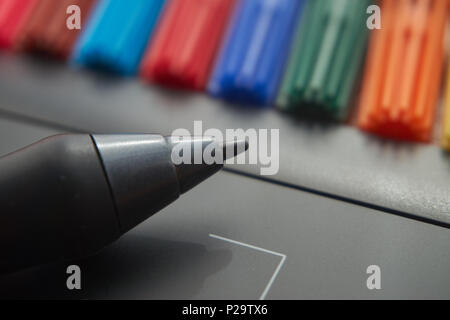 Black stylus pen on digital graphic tablet for illustrators and designers with colored markers in background. Macro view, free space and selective foc Stock Photo