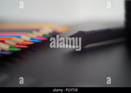 Digital stylus pen on digital graphic tablet for illustrators and designers with coloured pencils in background. Macro view, free space and selective  Stock Photo