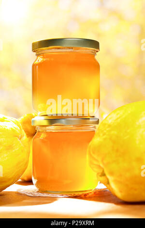 Quince jelly in glass jars with quinces on a wooden table in bright sunshine in front of an yellow and orange background. Stock Photo