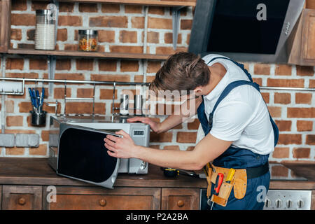 professional young foreman repairing microwave oven in kitchen Stock Photo