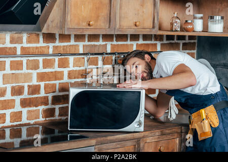young handyman repairing microwave oven in kitchen Stock Photo
