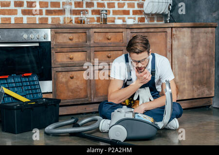 young repairman in protective glasses looking at broken vacuum cleaner Stock Photo