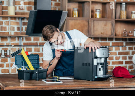 professional young worker in eyeglasses and protective workwear fixing coffee machine Stock Photo