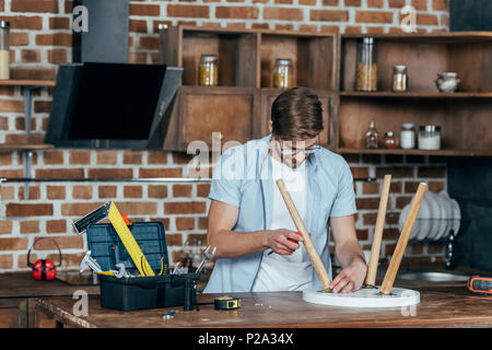 focused young man in eyeglasses holding screwdriver and repairing stool with screwdriver Stock Photo