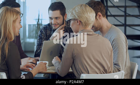 Group of five people discussing something with smile while sitting at the office table Stock Photo