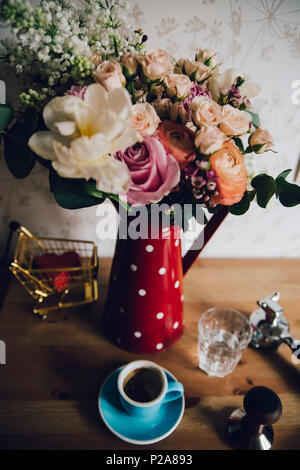 Beautiful flower bouquet of white lilac, roses, peony, ranunculus, eucalyptus, fresh morning espresso coffee in a blue cup with a saucer Stock Photo