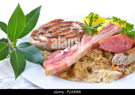 Belly of pork and various sausages on sauerkraut with boiled potatoes, white background Stock Photo