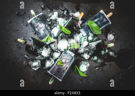 Trendy food, Asian vegan desserts, homemade ice cream popsicles with algae spirulina, served with mint in glasses with ice, dark rusty background copy Stock Photo