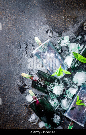 Trendy food, Asian vegan desserts, homemade ice cream popsicles with algae spirulina, served with mint in glasses with ice, dark rusty background copy Stock Photo