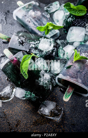 Trendy food, Asian vegan desserts, homemade ice cream popsicles with algae spirulina, served with mint in glasses with ice, dark rusty background copy Stock Photo
