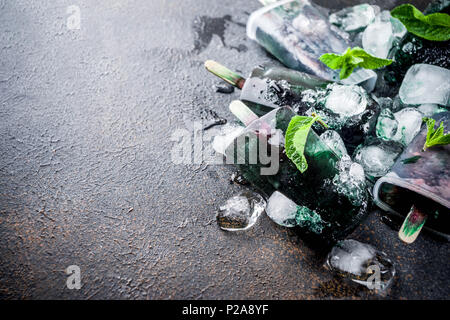 Trendy food, Asian vegan desserts, homemade ice cream popsicles with algae spirulina, served with mint in glasses with ice, dark rusty background copy Stock Photo