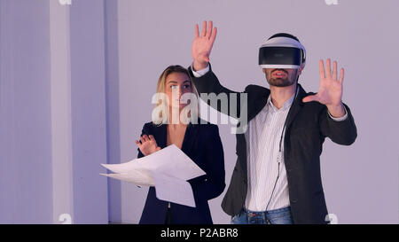 Young female architect with blueprints discissing construction project with her partner in vr headset Stock Photo