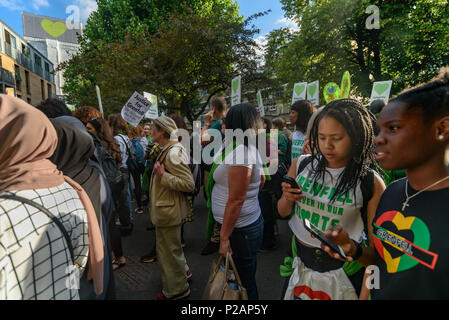 London, UK. 14th June 2018. Grenfell Tower, now covered and with a heart on its top looms over people gathering to walk in silence from close to Grenfell Tower remembering the victims of the disaster on the first anniversary of the disastrous fire which killed 72 and left survivors traumatised. Many of those made homeless by the fire are still in temporary accomodation a year later despite promises mde by Theresa May and Kensington & Chelsea council, who many fell have failed the local community both before and after the fire. They say had they been listened to and respected Grenfell would not Stock Photo