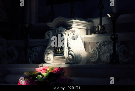 The stone altar of a dark church, lightened up by an outside ray of natural light, with flowers and mystic symbols. Religious, sacred symbolic shot. Stock Photo