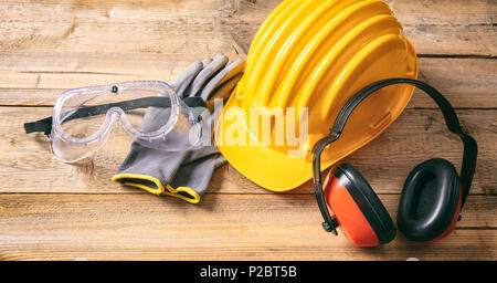 Construction site safety. Protective hard hat, headphones, gloves and glasses on wooden background Stock Photo
