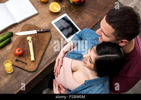 overhead view of happy young pregnant couple embracing while cooking together Stock Photo