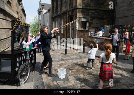 Street entertainer blowing large soap bubbles with children watching; Edinburgh old town, Edinburgh Scotland UK Stock Photo