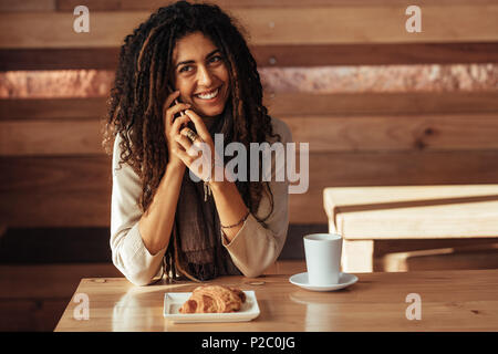 Woman sitting in a restaurant talking on mobile phone. Smiling woman at a cafe with coffee and snacks on the table. Stock Photo