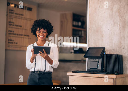 Portrait of female manager in restaurant with digital tablet. Beautiful young african business woman in restaurant using digital tablet. Stock Photo