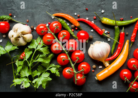 Hot chili peppers multi-colored, tomato cherry on branch, garlic and other spices on black background. Stock Photo