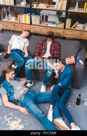 high angle view of young multiethnic friends sleeping in messy room with popcorn and beer bottles Stock Photo