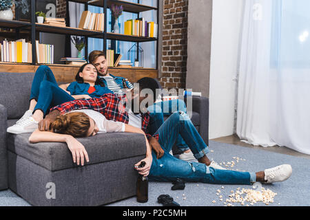 young multiethnic friends sleeping in messy room with popcorn and beer bottles Stock Photo