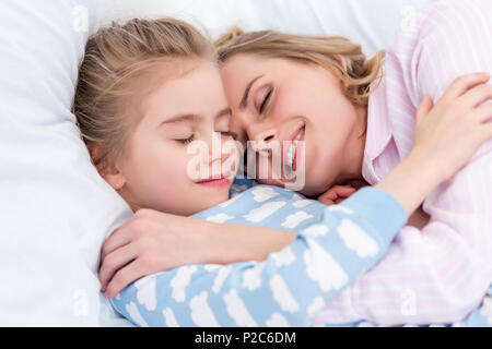 beautiful mother and daughter hugging and sleeping together in bed