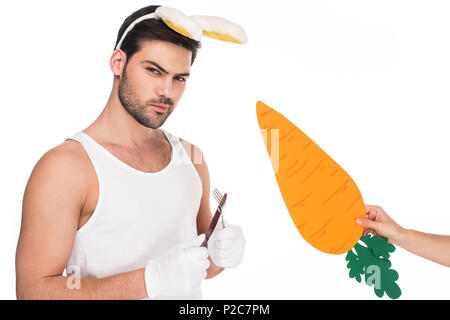 Man with bunny ears holding cutlery while female hand holding carrot beside isolated on white, easter concept Stock Photo