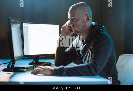hacker with program on computer calling on cell Stock Photo